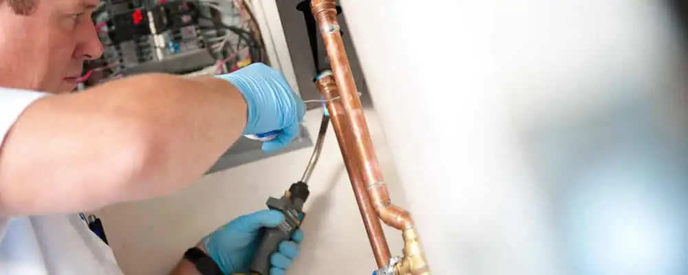 Water heater repair technician testing copper pipe connections and controls in Houston, TX